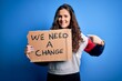 © Krakenimages.com - Young beautiful activist woman holding banner with change message over blue background very happy pointing with hand and finger