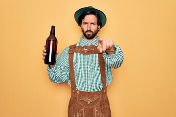 Wall Mural - Young handsome man wearing tratidional german octoberfest custome and drinking beer from bottle pointing with finger to the camera and to you, hand sign, positive and confident gesture from the front