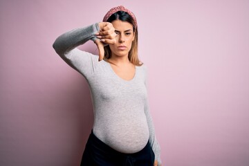 Canvas Print - Young beautiful brunette woman pregnant expecting baby over isolated pink background looking unhappy and angry showing rejection and negative with thumbs down gesture. Bad expression.