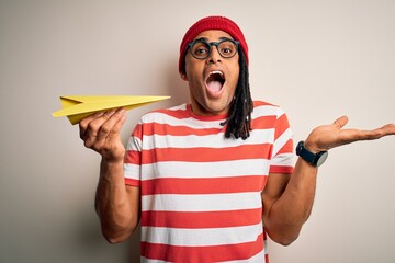 Wall Mural - Young african american afro man with dreadlocks holding paper airplane very happy and excited, winner expression celebrating victory screaming with big smile and raised hands