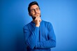 © Krakenimages.com - Young handsome man with beard wearing casual sweater and glasses over blue background looking confident at the camera smiling with crossed arms and hand raised on chin. Thinking positive.