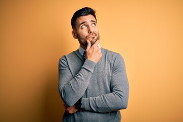 Wall Mural - Young handsome businessman wearing elegant sweater and tie over yellow background with hand on chin thinking about question, pensive expression. Smiling with thoughtful face. Doubt concept.