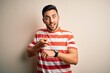 © Krakenimages.com - Young handsome man wearing casual striped t-shirt standing over isolated white background In hurry pointing to watch time, impatience, upset and angry for deadline delay