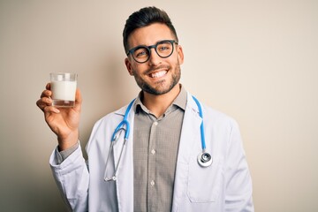 Young doctor man wearing stethoscope holding a glass of milk over isolated background with a happy face standing and smiling with a confident smile showing teeth