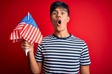 Poster - Young handsome patriotic man holding united states flags celebrating independence day scared in shock with a surprise face, afraid and excited with fear expression