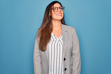 Sticker - Young hispanic business woman wearing glasses standing over blue isolated background looking away to side with smile on face, natural expression. Laughing confident.