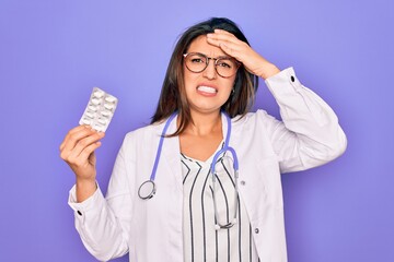 Sticker - Young professional doctor woman holding pharmaceutical pills over purple background stressed with hand on head, shocked with shame and surprise face, angry and frustrated. Fear and upset for mistake.