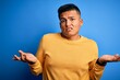 © Krakenimages.com - Young handsome latin man wearing yellow casual sweater over isolated blue background clueless and confused with open arms, no idea concept.