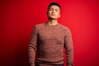 © Krakenimages.com - Young handsome latin man wearing casual sweater standing over red background Relaxed with serious expression on face. Simple and natural looking at the camera.