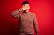 © Krakenimages.com - Young handsome latin man wearing casual sweater standing over red background smiling and laughing with hand on face covering eyes for surprise. Blind concept.