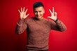 © Krakenimages.com - Young handsome latin man wearing casual sweater standing over red background showing and pointing up with fingers number eight while smiling confident and happy.