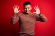 © Krakenimages.com - Young handsome latin man wearing casual sweater standing over red background showing and pointing up with fingers number nine while smiling confident and happy.