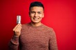 © Krakenimages.com - Young handsome latin man holding led lightbulb over isolated red background with a happy face standing and smiling with a confident smile showing teeth