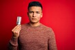 © Krakenimages.com - Young handsome latin man holding led lightbulb over isolated red background with a confident expression on smart face thinking serious