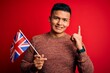 © Krakenimages.com - Young handsome latin patriotic man wearing united kingdom flag over red background surprised with an idea or question pointing finger with happy face, number one