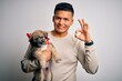 © Krakenimages.com - Young handsome latin man holding cute puppy pet over isolated white background doing ok sign with fingers, excellent symbol