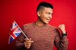 © Krakenimages.com - Young handsome latin patriotic man wearing united kingdom flag over red background pointing and showing with thumb up to the side with happy face smiling