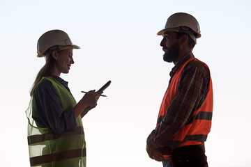 Wall Mural - An engineer wearing a hard hat and holding a tablet stands in front of a worker on an isolated white background