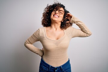 Poster - Young beautiful curly arab woman wearing casual t-shirt and glasses over white background stretching back, tired and relaxed, sleepy and yawning for early morning