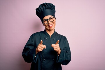 Poster - Middle age brunette chef woman wearing cooker uniform and hat over isolated pink background pointing fingers to camera with happy and funny face. Good energy and vibes.