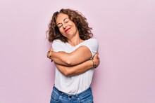 Middle Age Beautiful Woman Wearing Casual T-shirt Standing Over Isolated Pink Background Hugging Oneself Happy And Positive, Smiling Confident. Self Love And Self Care