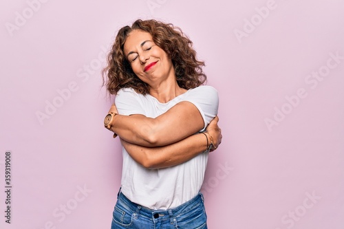 Fotografía Middle age beautiful woman wearing casual t-shirt standing over isolated pink background hugging oneself happy and positive, smiling confident