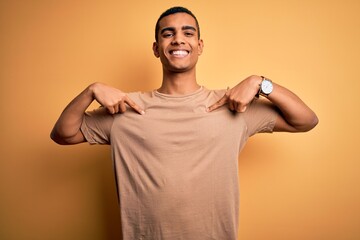 Wall Mural - Young handsome african american man wearing casual t-shirt standing over yellow background looking confident with smile on face, pointing oneself with fingers proud and happy.