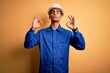 © Krakenimages.com - Young handsome african american worker man wearing blue uniform and security helmet relax and smiling with eyes closed doing meditation gesture with fingers. Yoga concept.