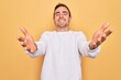 © Krakenimages.com - Young handsome man with blue eyes wearing casual sweater standing over yellow background smiling cheerful offering hands giving assistance and acceptance.