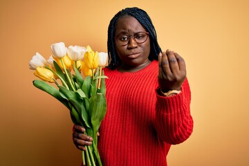 Canvas Print - Young african american plus size woman with braids holding bouquet of yellow tulips flower Doing Italian gesture with hand and fingers confident expression