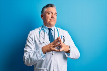 Poster - Middle age handsome grey-haired doctor man wearing coat and blue stethoscope Hands together and fingers crossed smiling relaxed and cheerful. Success and optimistic