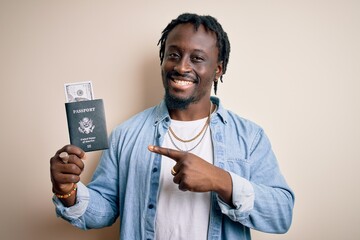 Wall Mural - Young african american tourist man holding passport with dollars banknotes as money travel very happy pointing with hand and finger