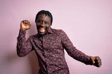 Sticker - Young handsome african american man wearing casual shirt standing over pink background Dancing happy and cheerful, smiling moving casual and confident listening to music