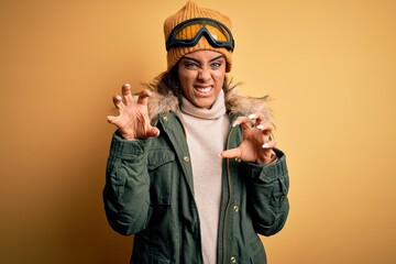 Wall Mural - Young african american afro skier girl wearing snow sportswear and ski goggles smiling funny doing claw gesture as cat, aggressive and sexy expression