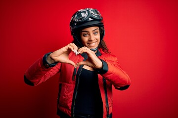 Sticker - Young african american motorcyclist girl wearing moto helmet and glasses over red background smiling in love showing heart symbol and shape with hands. Romantic concept.