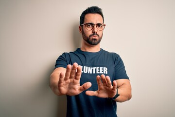 Wall Mural - Handsome man with beard wearing t-shirt with volunteer message over white background Moving away hands palms showing refusal and denial with afraid and disgusting expression. Stop and forbidden.