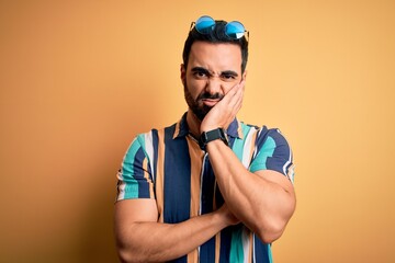 Handsome tourist man with beard on vacation wearing summer striped shirt and sunglasses thinking looking tired and bored with depression problems with crossed arms.