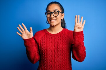 Poster - Young beautiful asian woman wearing casual sweater and glasses over blue background showing and pointing up with fingers number nine while smiling confident and happy.