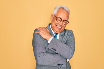 Poster - Middle age senior grey-haired handsome business man wearing glasses over yellow background Hugging oneself happy and positive, smiling confident. Self love and self care