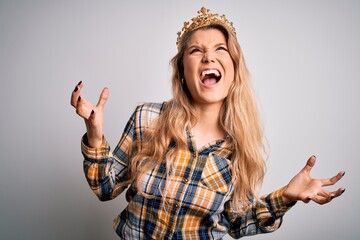 Sticker - Young beautiful blonde woman wearing golden crown of queen over isolated white background crazy and mad shouting and yelling with aggressive expression and arms raised. Frustration concept.