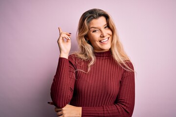 Sticker - Young beautiful blonde woman wearing casual sweater over isolated pink background with a big smile on face, pointing with hand and finger to the side looking at the camera.