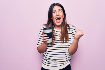 Young beautiful brunette woman drinking cup of takeaway coffee over isolated pink background screaming proud, celebrating victory and success very excited with raised arm