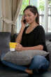 © bongkarn - Young female sitting on black sofa in living room and talking on the phone to someone while holding a cup