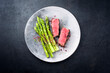 Gegrilltes dry aged Wagyu Roastbeef Steak vom Rind mit grünen Spargel und Kräuter als Draufsicht auf einem Modern Design Teller mit Textfreiraum