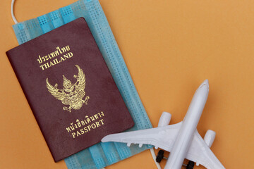 Thai Passport with medical face mask and airplane on pale coral background with copy space. Lifestyle and traveling concept in New Normal after Covid-19 / Coronavirus pandemic.