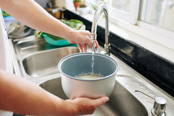 Hands of person pouring tap water in bowl with rice to rinse it