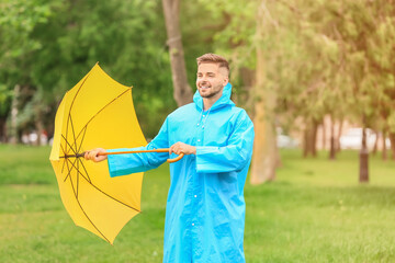 Wall Mural - Young man with umbrella wearing raincoat outdoors