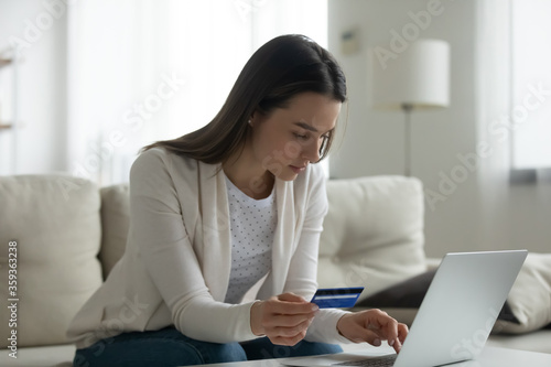 Cuadros en Lienzo Serious woman sit on sofa typing on laptop holding plastic credit card using sec