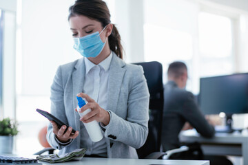 Businesswoman disinfecting her smart phone in the office.	