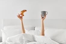 Morning, Comfort And People Concept - Young Woman With Cup Of Coffee And Croissant Lying In Bed At Home Bedroom